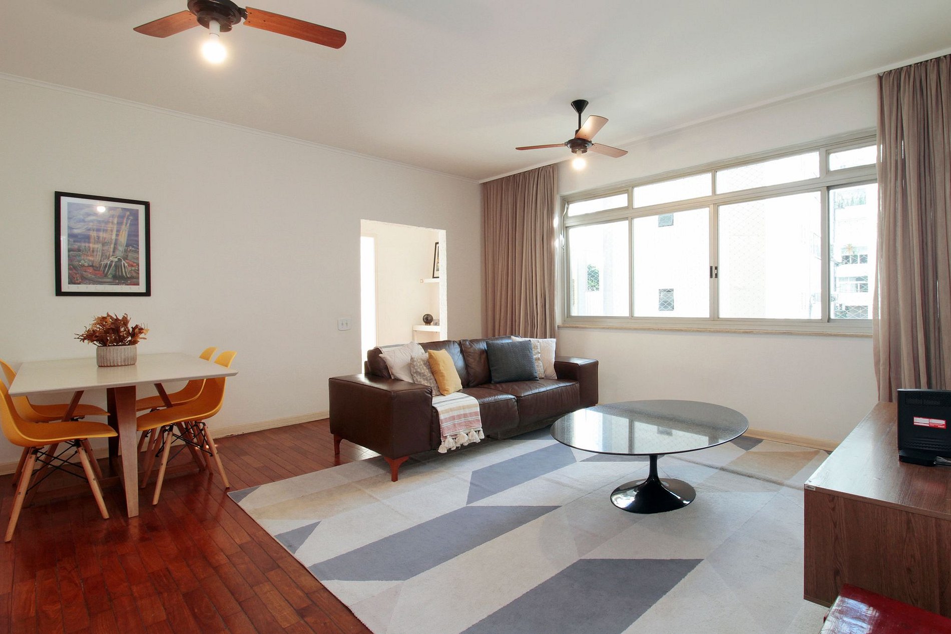 Sala do apartamento, com amplas janelas, piso de madeira e área de jantar